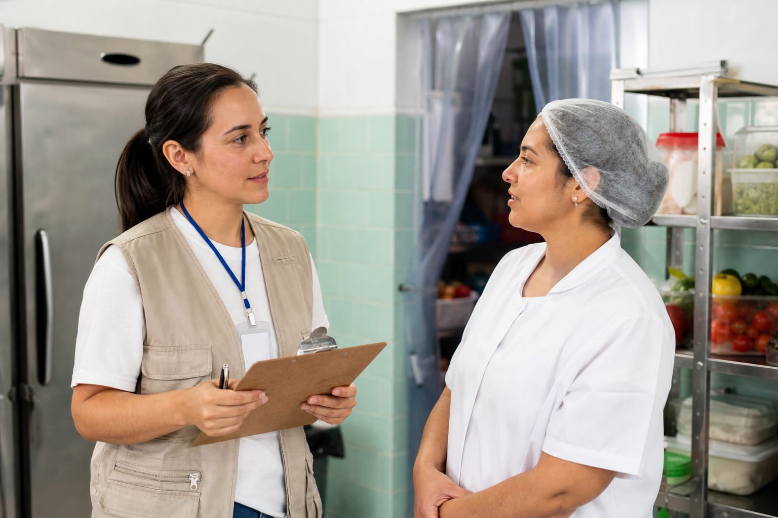 Fiscal com prancheta conversa com nutricionista dentro da cozinha de uma casa de repouso